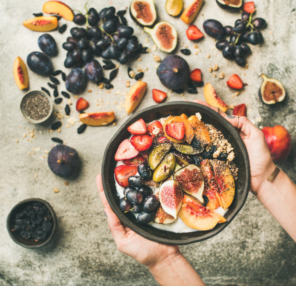 Healthy breakfast bowl in hands of woman, top view